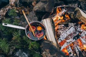pexels-photo-6176683-6176683 Pot of mulled wine simmering over a campfire outdoors with oranges and spices.